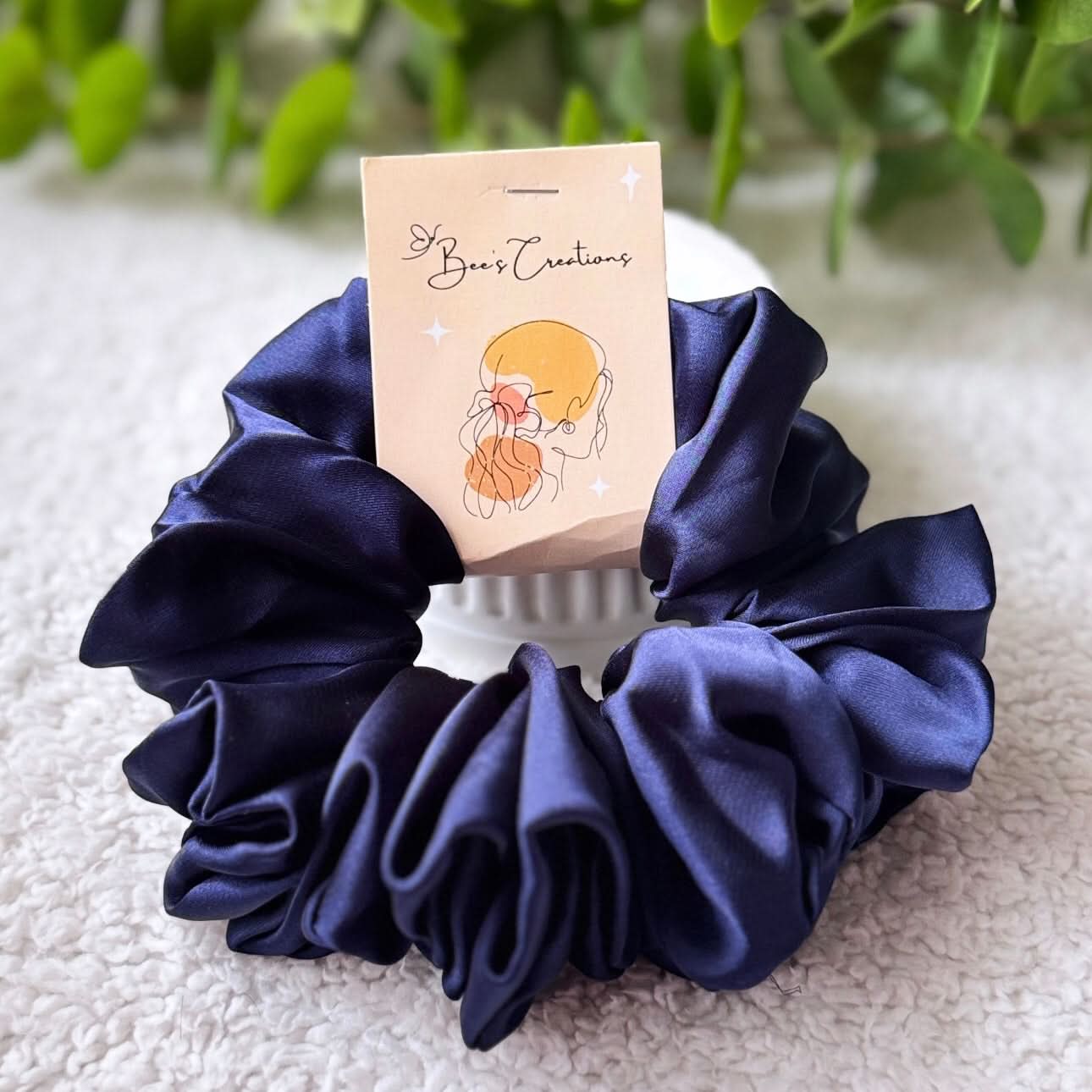 Navy blue scrunchie with a branded card on a textured surface