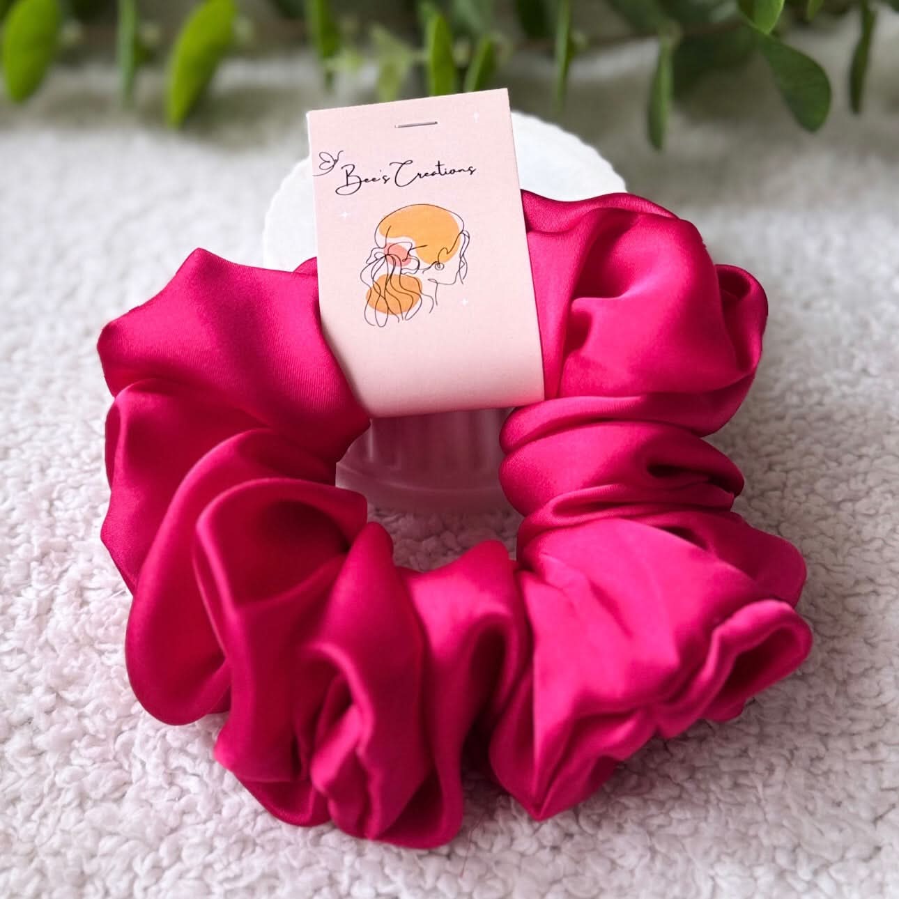 Pink scrunchie on a white stand with a small card on a light background