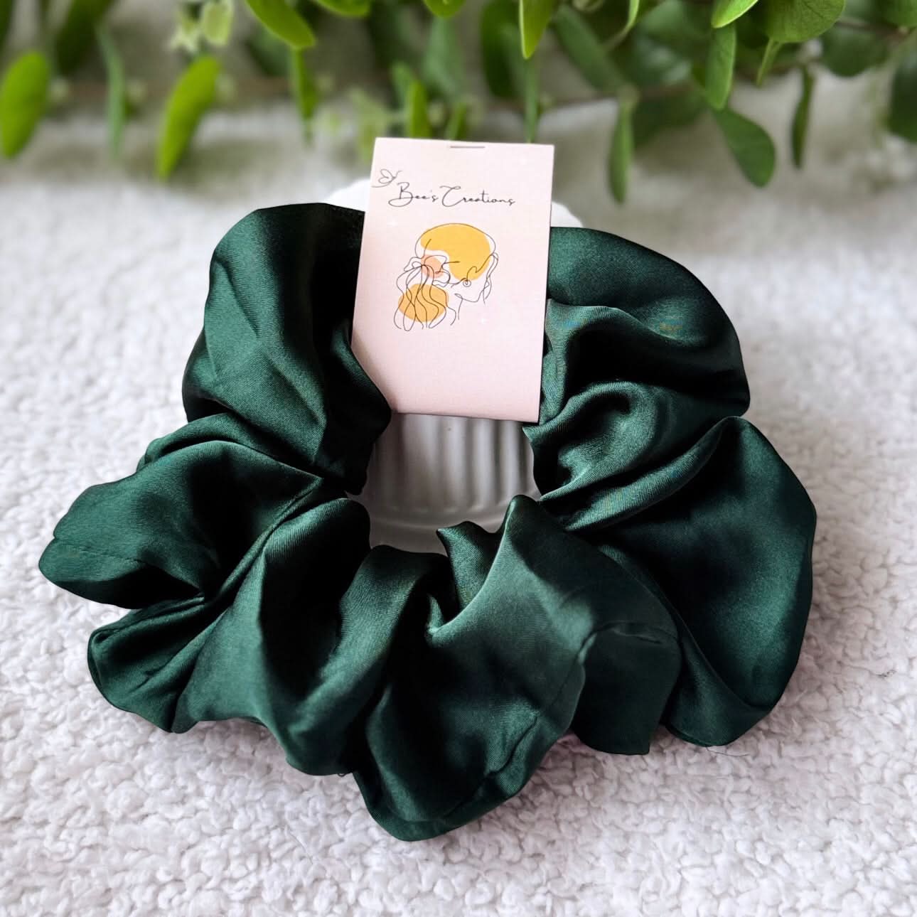 Green satin scrunchie with a card on a textured surface with plants in the background