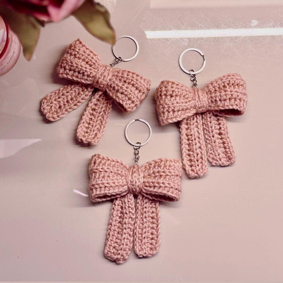 Three pink crocheted bow keychains on a light pink background
