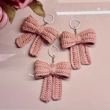 Three pink crocheted bow keychains on a light pink background