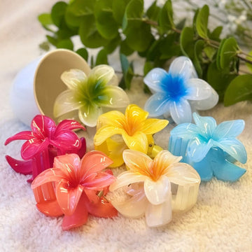 Colorful flower-shaped hair clips on a textured surface with green leaves in the background