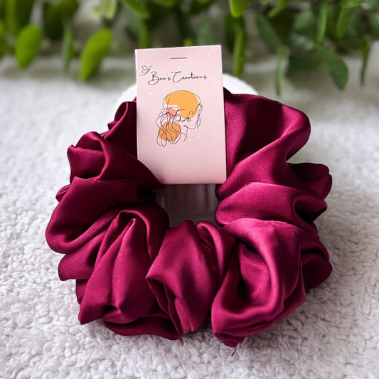 Maroon scrunchie with a card on a textured surface with greenery in the background