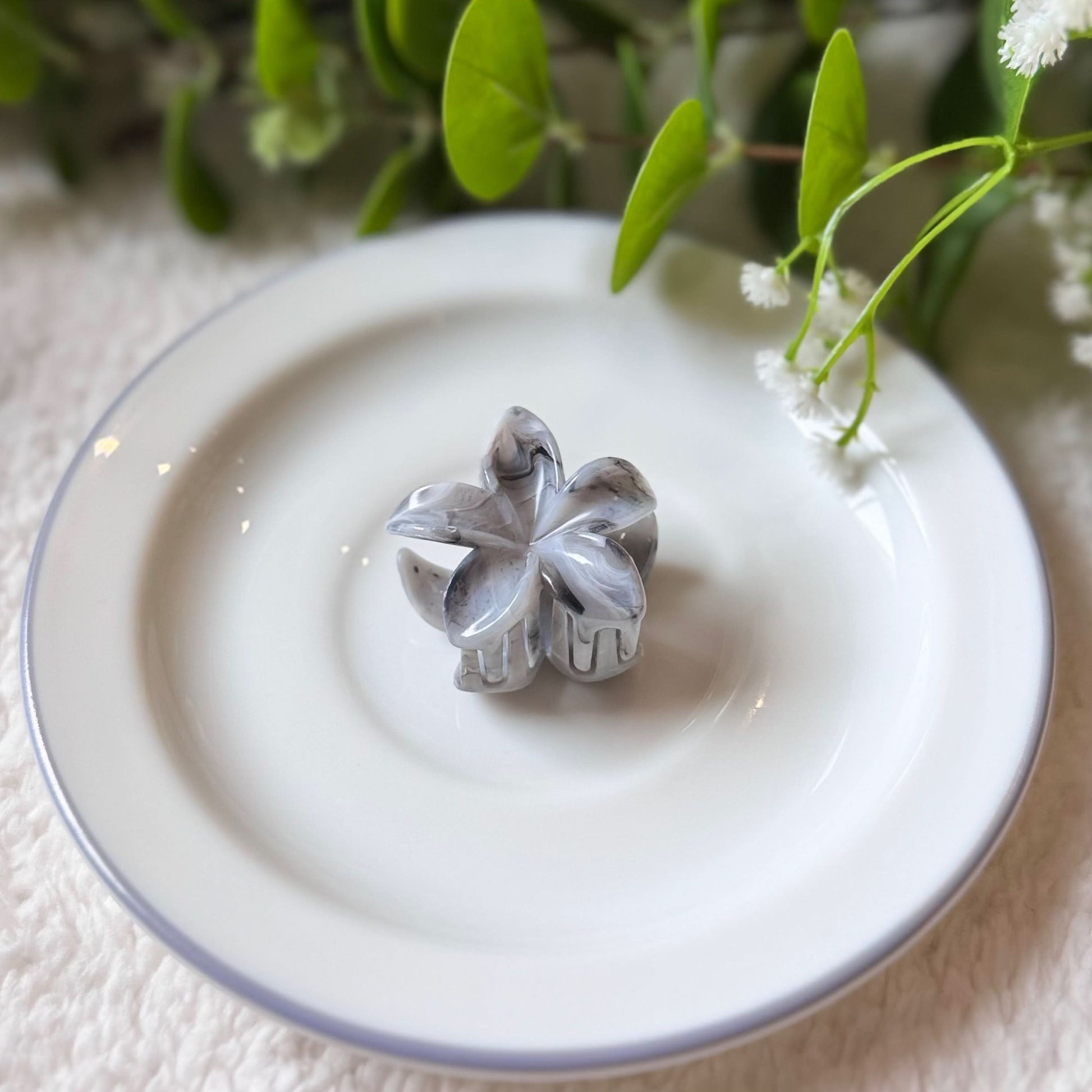 Metallic four-leaf clover ornament on a white plate with greenery in the background