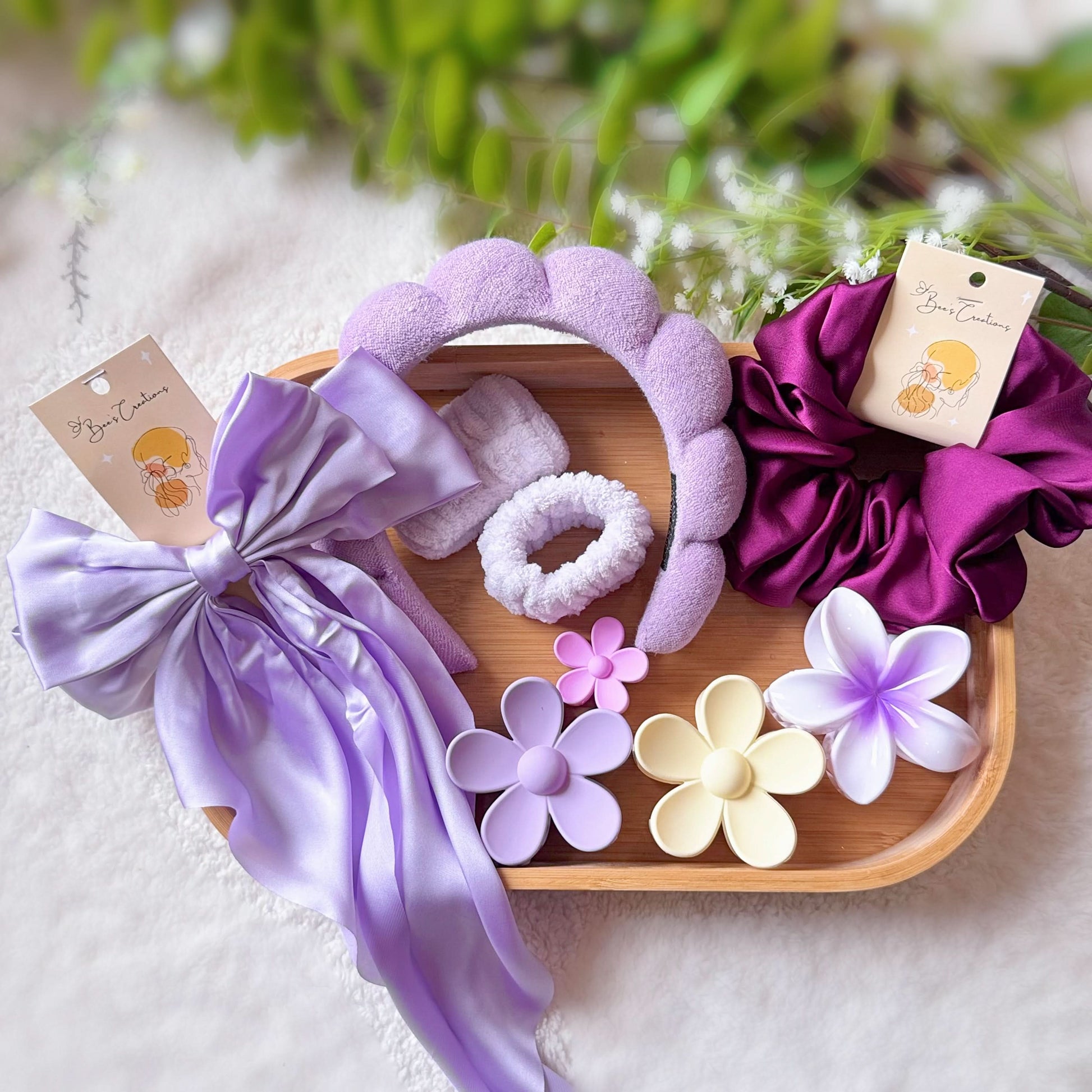 Set of purple hair accessories including headbands and scrunchies on a wooden tray with decorative flowers.