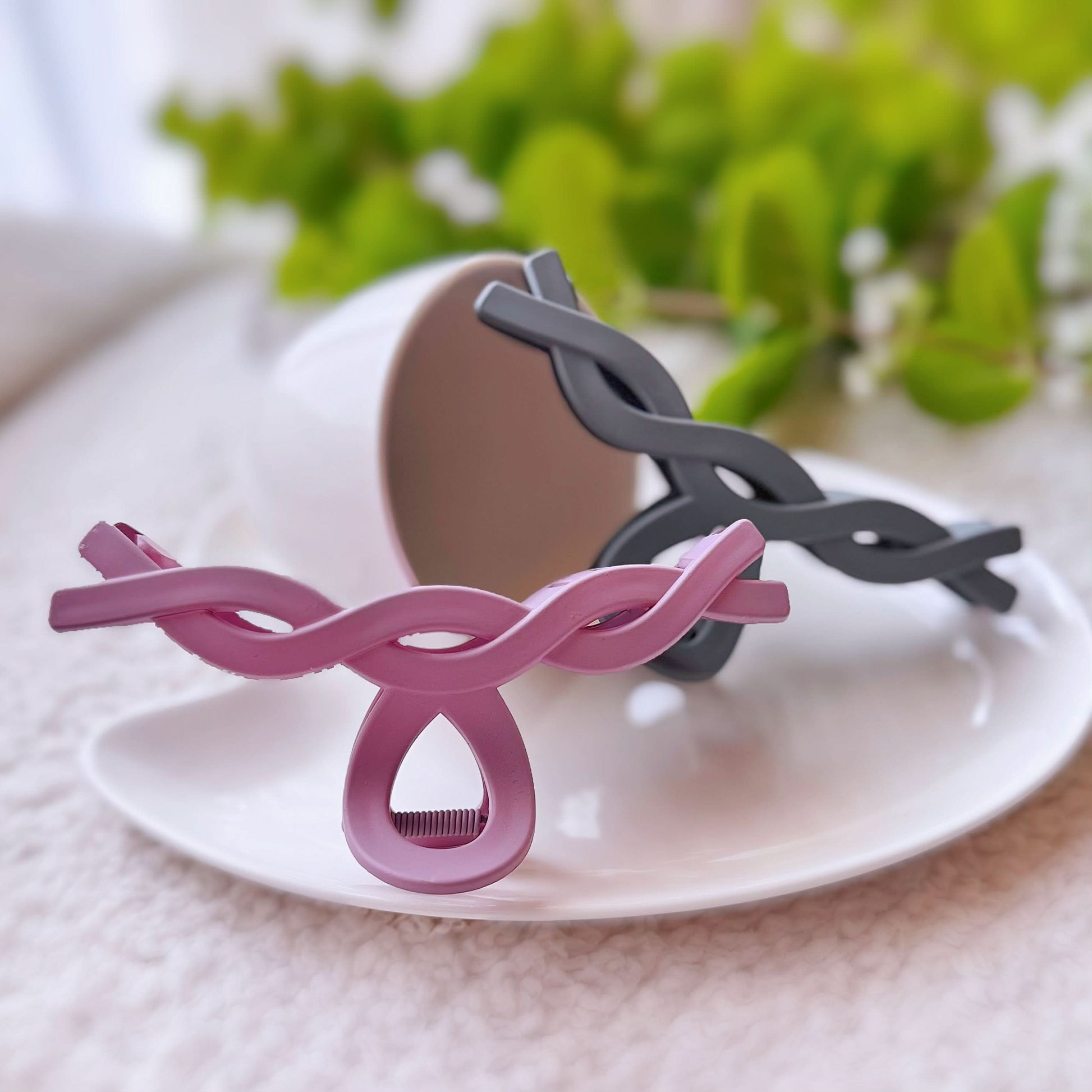 Pink and black hair clip on a white plate with greenery in the background