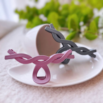 Pink and black hair clip on a white plate with greenery in the background