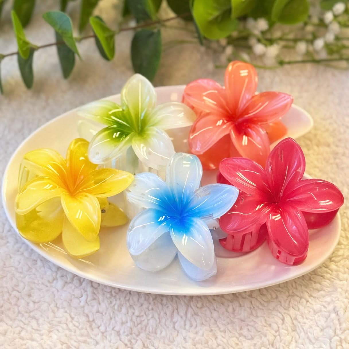 Colorful flower-shaped hair clips on a white plate with green leaves in the background