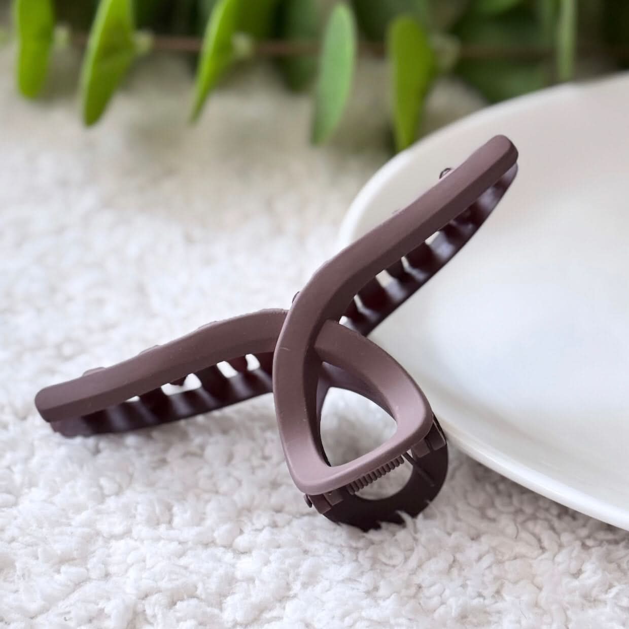 Brown hair clip on a textured surface with green leaves in the background