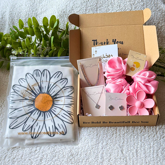Gift box with jewelry and pink flowers on a textured surface with greenery in the background