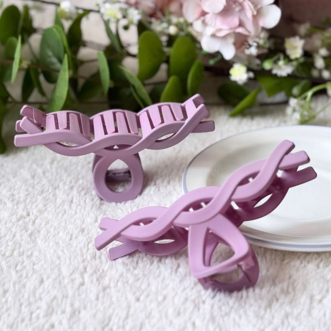 Two purple hairclips on a textured surface with flowers in the background
