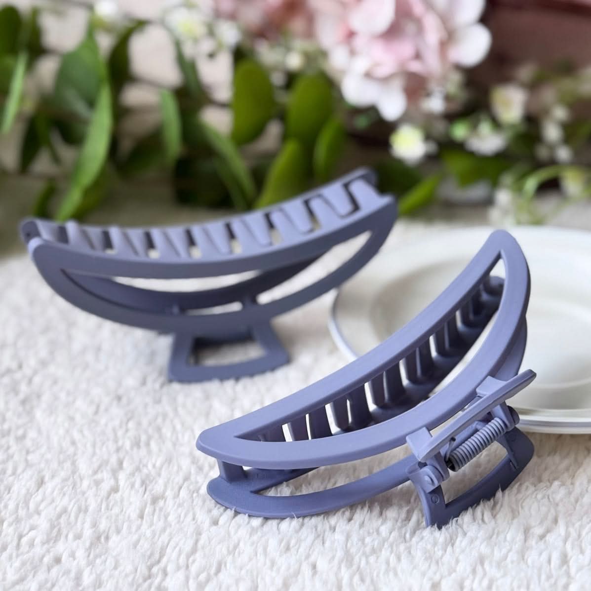 Two blue hair clips on a textured surface with flowers in the background