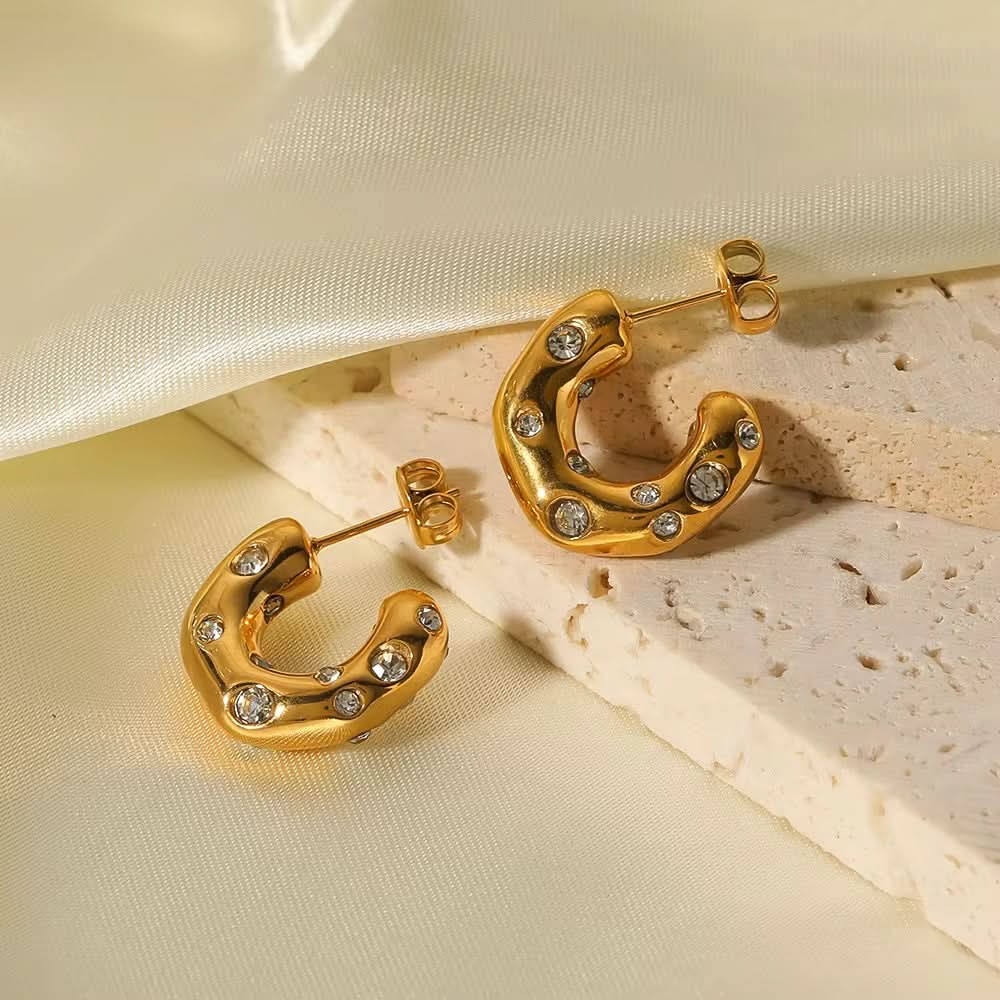 Gold hoop earrings with small diamonds on a beige fabric background
