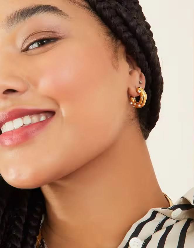 Close-up of a woman wearing gold hoop earrings with a neutral background