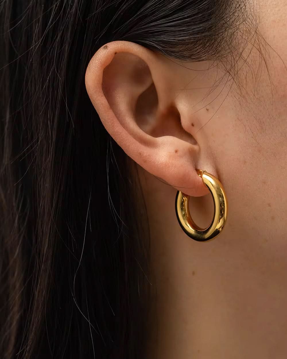 Gold hoop earring worn by a person with dark hair.