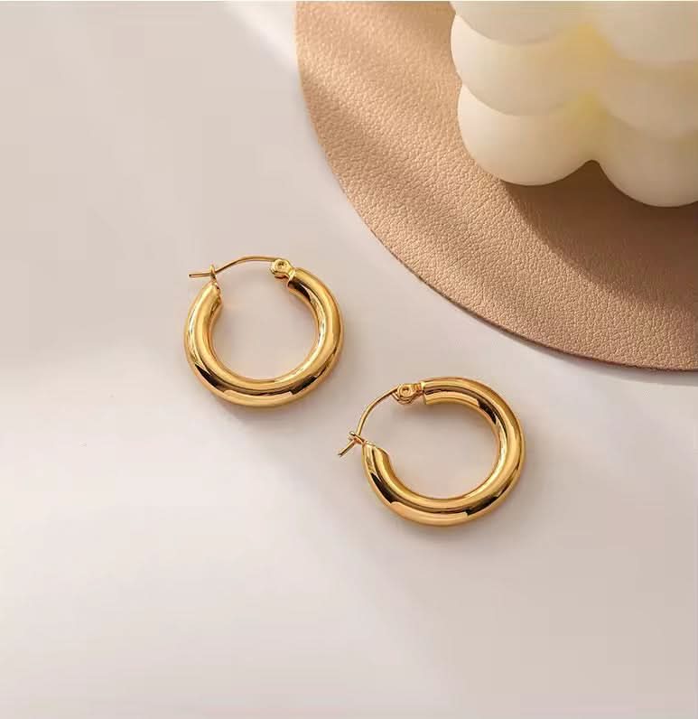 Gold hoop earrings on a light surface with a beige mat and white flowers in the background
