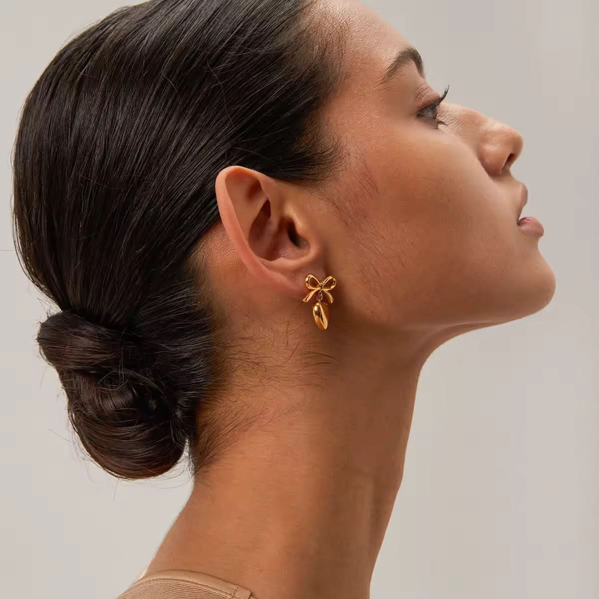 Woman wearing a gold bow-shaped earring against a neutral background