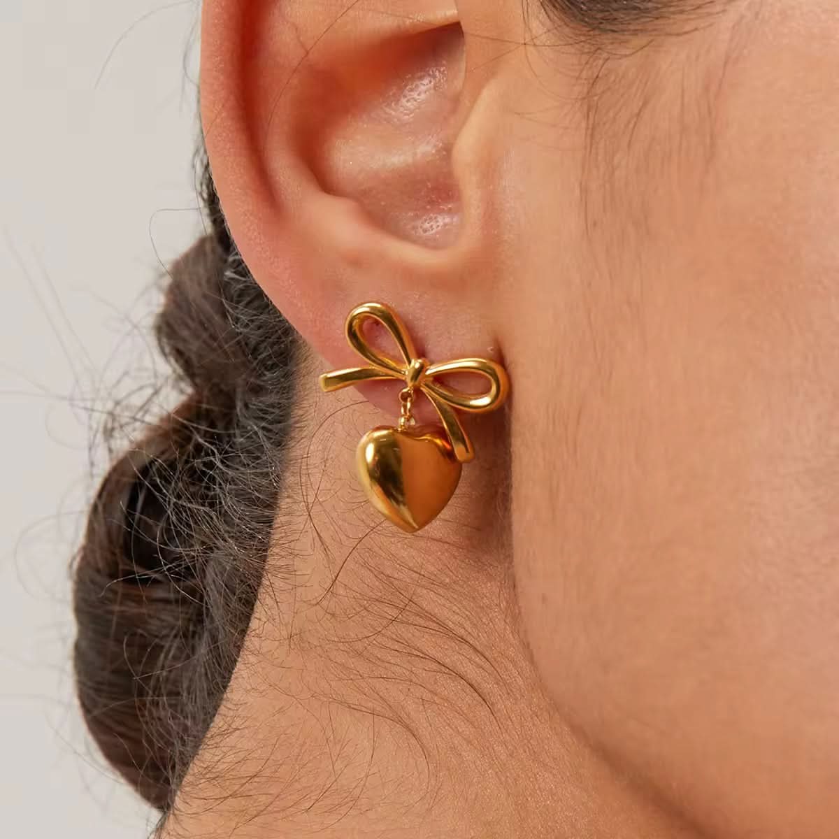 Gold bow-shaped earring worn on an ear with a neutral background