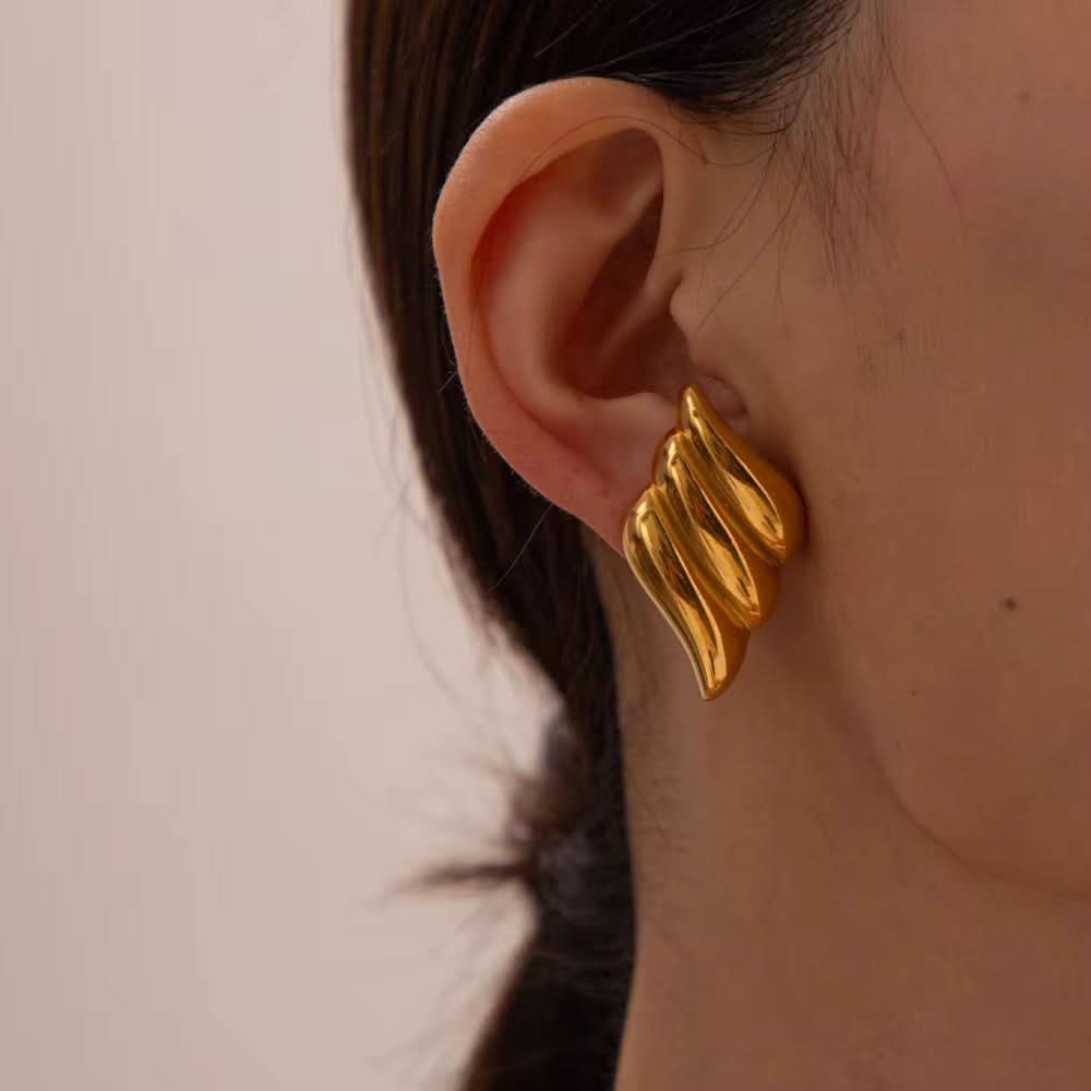 Gold wing-shaped earring worn by a person with a neutral background