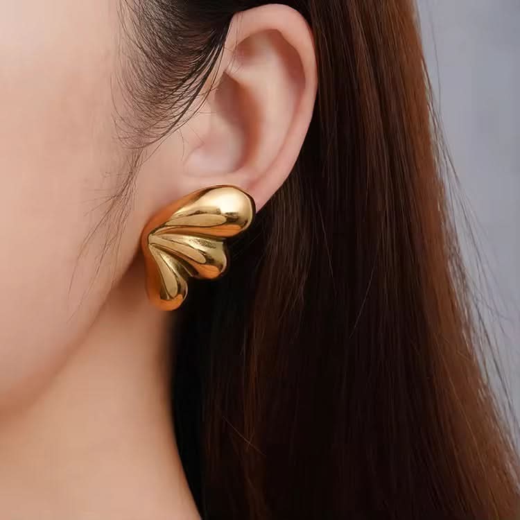 Gold heart-shaped earring worn by a person with dark hair.