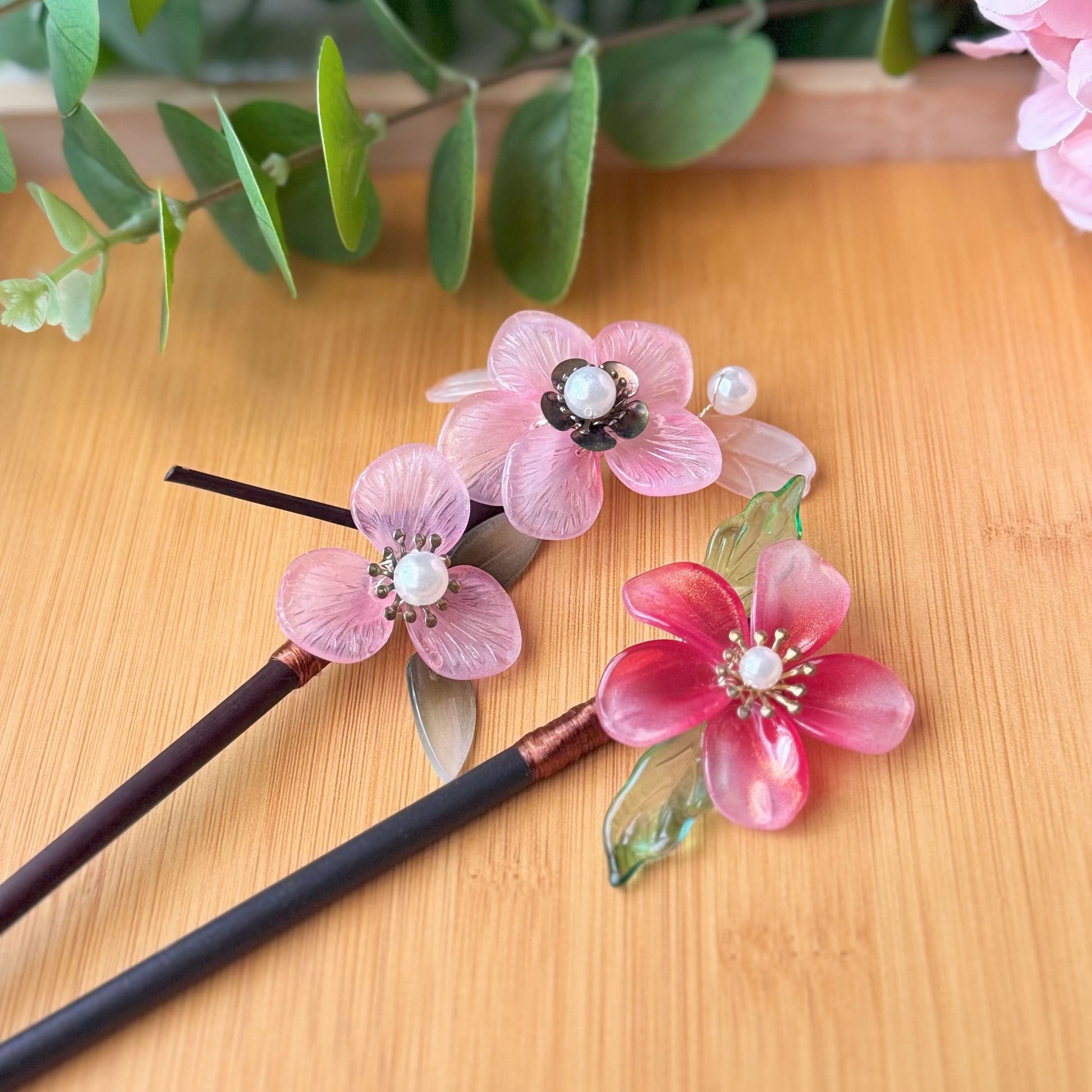 Decorative hair sticks with pink floral designs on a wooden surface