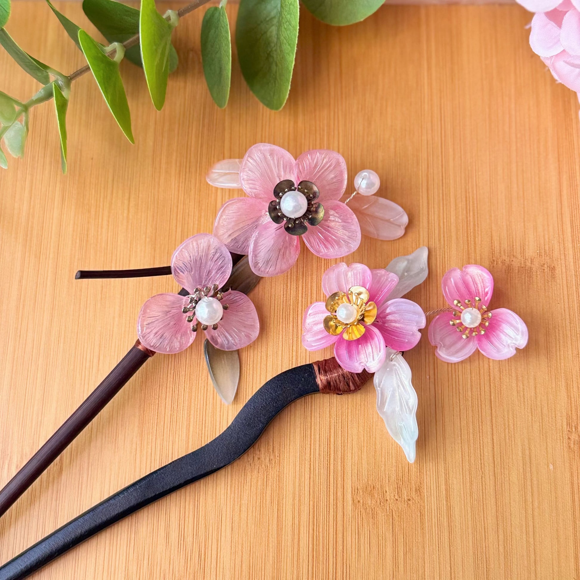 Decorative hair sticks with pink floral designs on a wooden surface