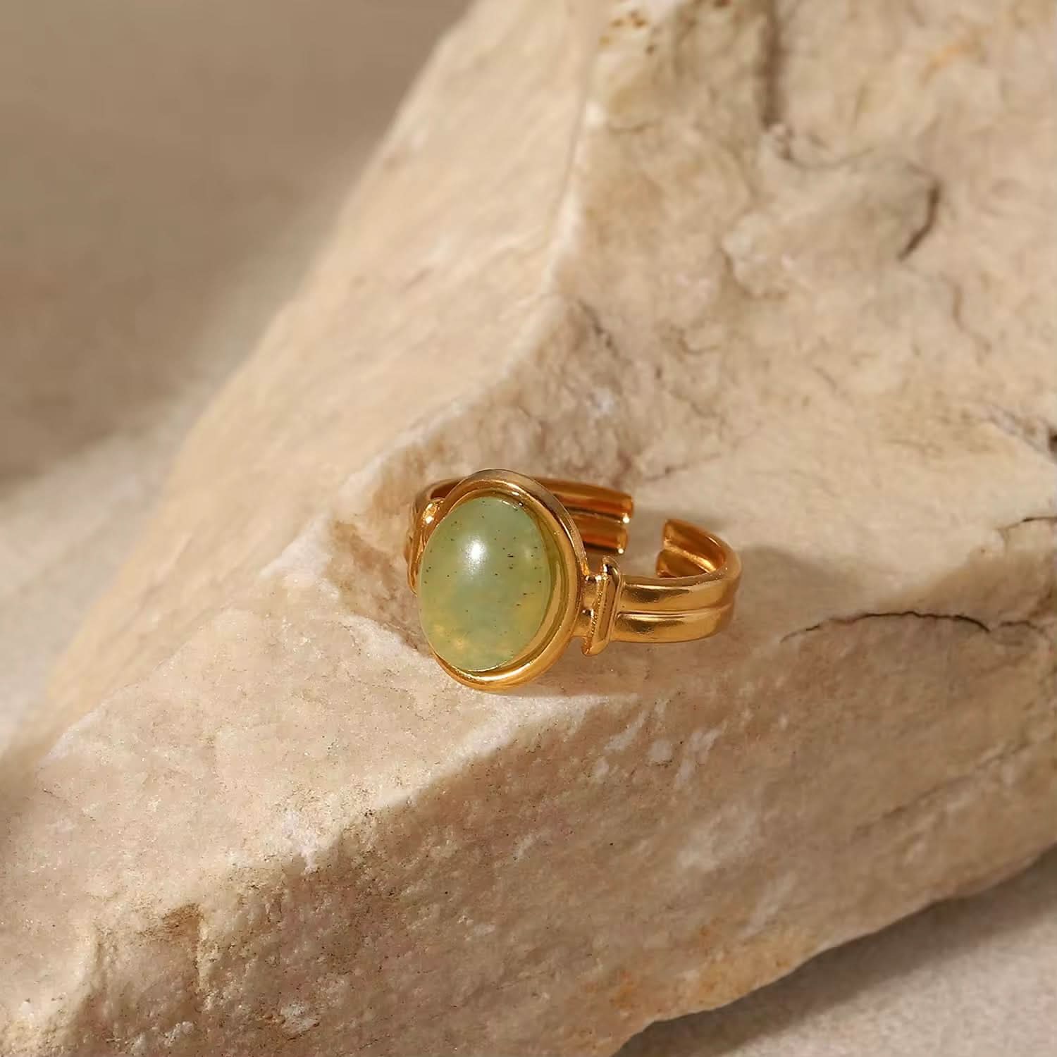 Gold ring with a green stone on a beige stone surface