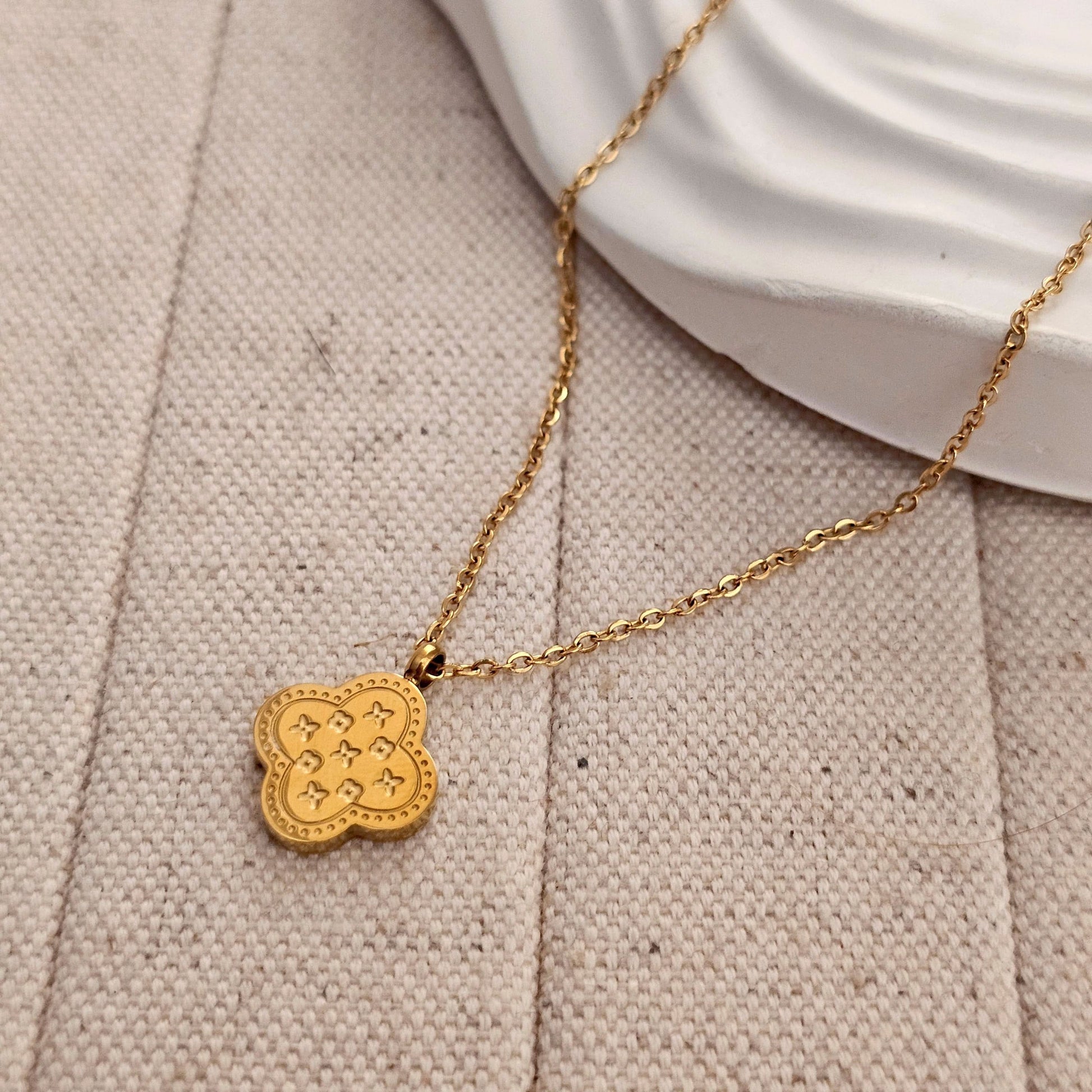 Gold necklace with a clover-shaped pendant on a beige fabric background