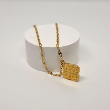Gold necklace with a clover shaped pendant on a white stand