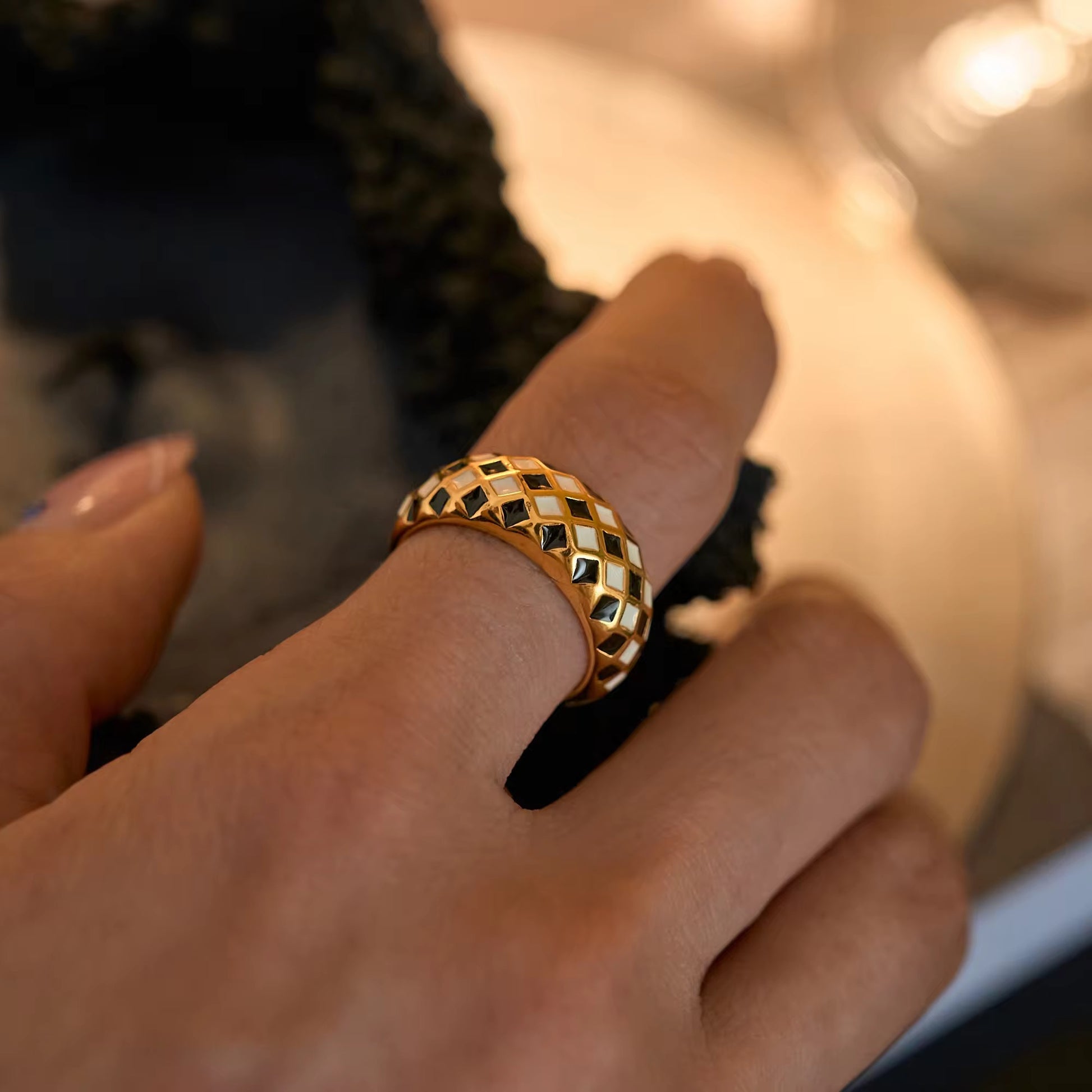 Gold ring with a black and white pattern worn on a finger against a blurred background
