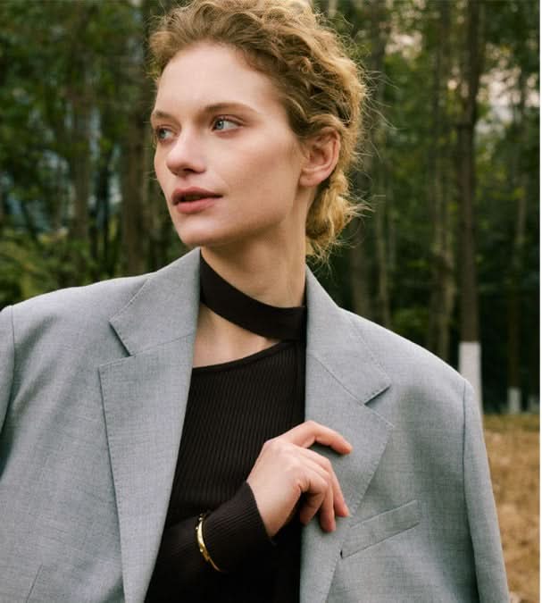 Woman wearing a gray blazer over a black top with a blurred natural background