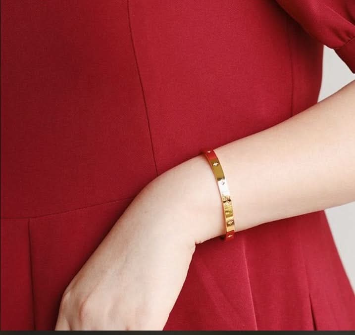 Gold bracelet on a wrist with a red garment in the background