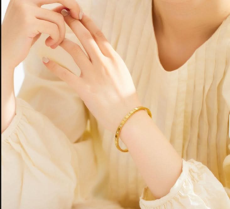 Close-up of a person wearing a gold bracelet on a blurred background