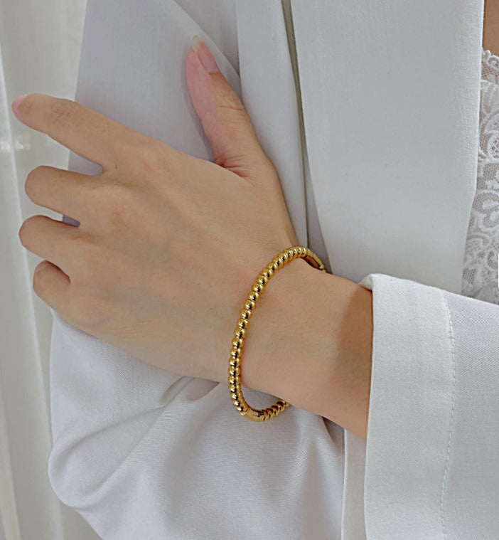 Gold bracelet on a wrist with a white background